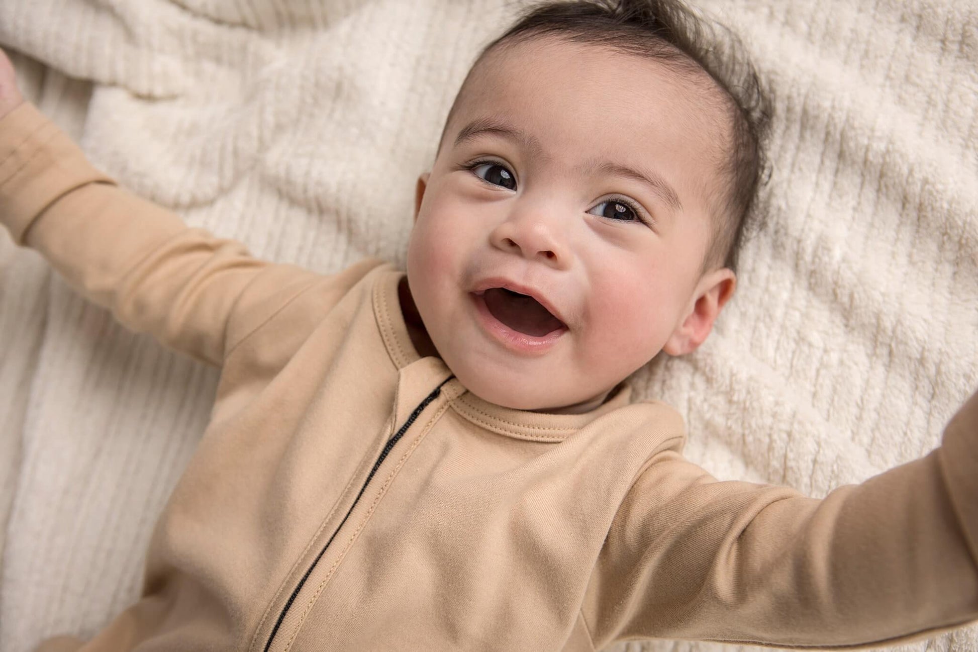 Baby less than 12 months old, laying down wearing a nueborn Khaki double zip sleepsuit