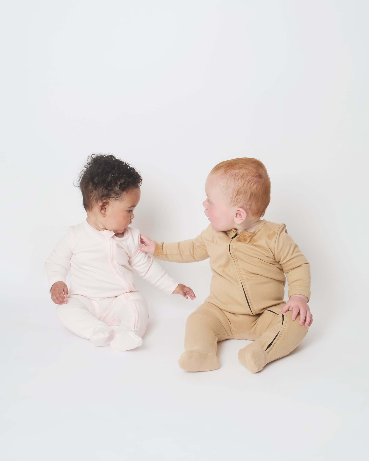 one baby touching another babies nueborn sleepsuit to feel its softness