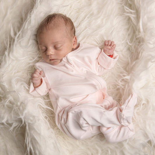 Baby less than 12 months old, asleep wearing a nueborn pink double zip sleepsuit