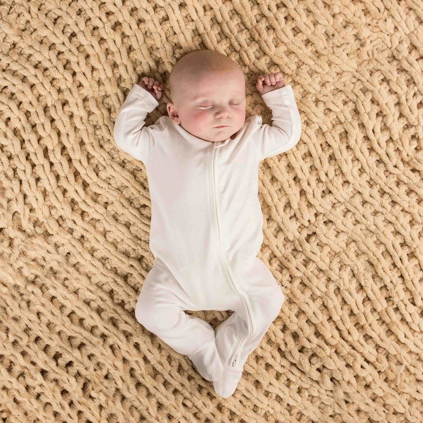 Baby less than 12 months old, laying down asleep wearing a nueborn white double zip sleepsuit